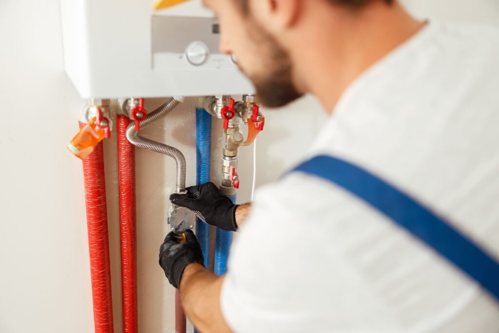 bearded plumber in blue overalls installing a hot water system pipe